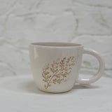 Handmade ceramic mug with a real leaf impression in sandy clay and a glossy white finish.