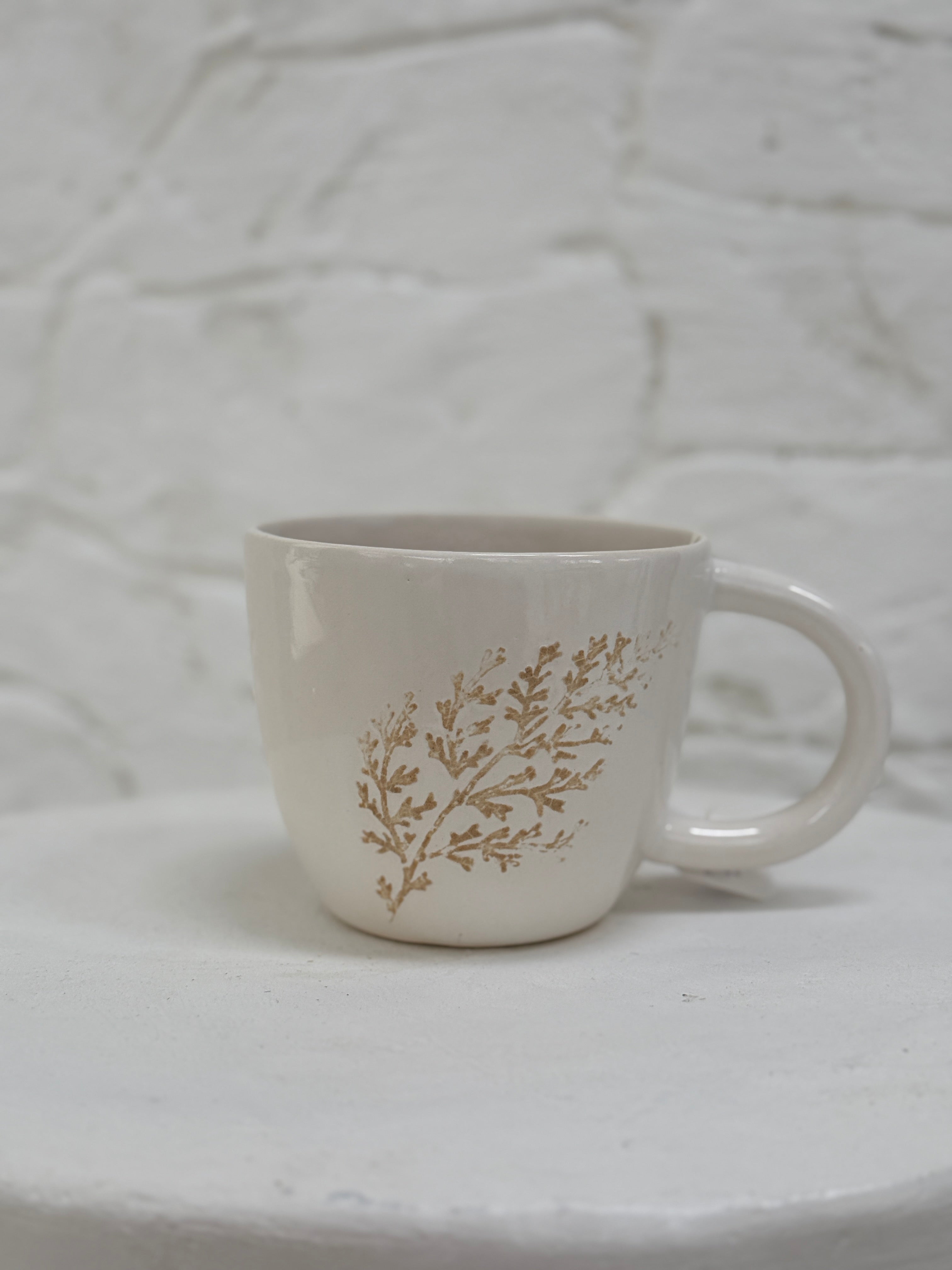 Handmade ceramic mug with a real leaf impression in sandy clay and a glossy white finish.