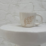 Handmade ceramic mug with a real leaf impression in sandy clay and a glossy white finish.