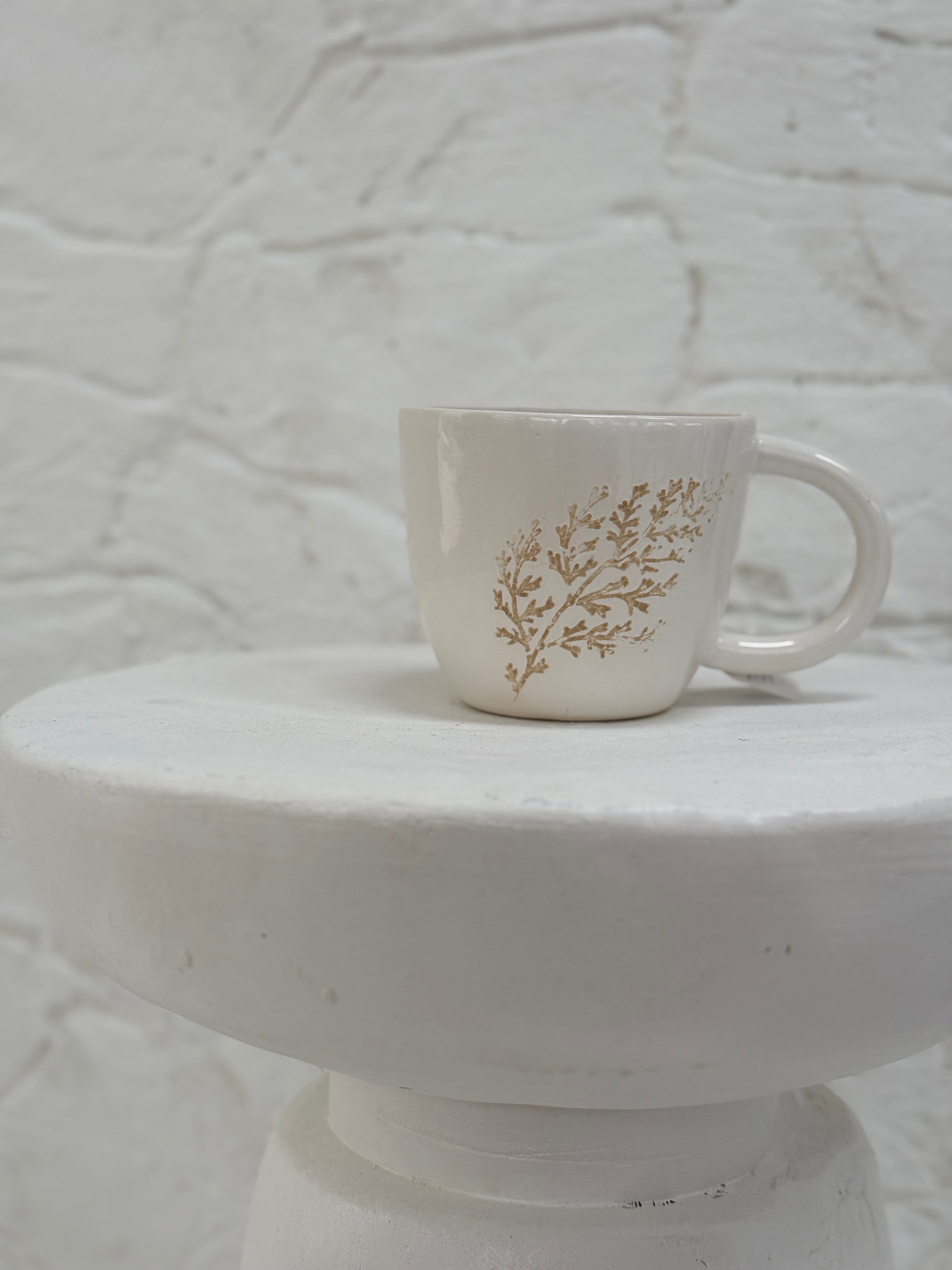Handmade ceramic mug with a real leaf impression in sandy clay and a glossy white finish.