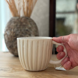 Handmade ceramic coffee mug with hand-carved vertical column lines and a glossy white interior.