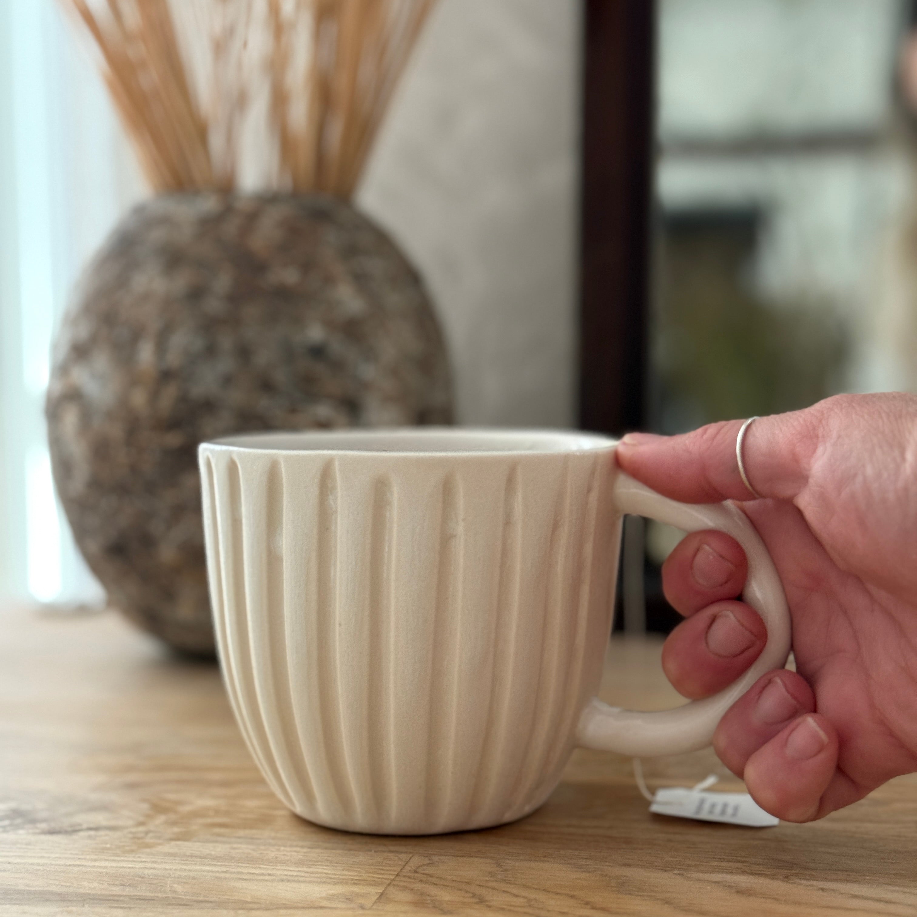 Handmade ceramic coffee mug with hand-carved vertical column lines and a glossy white interior.