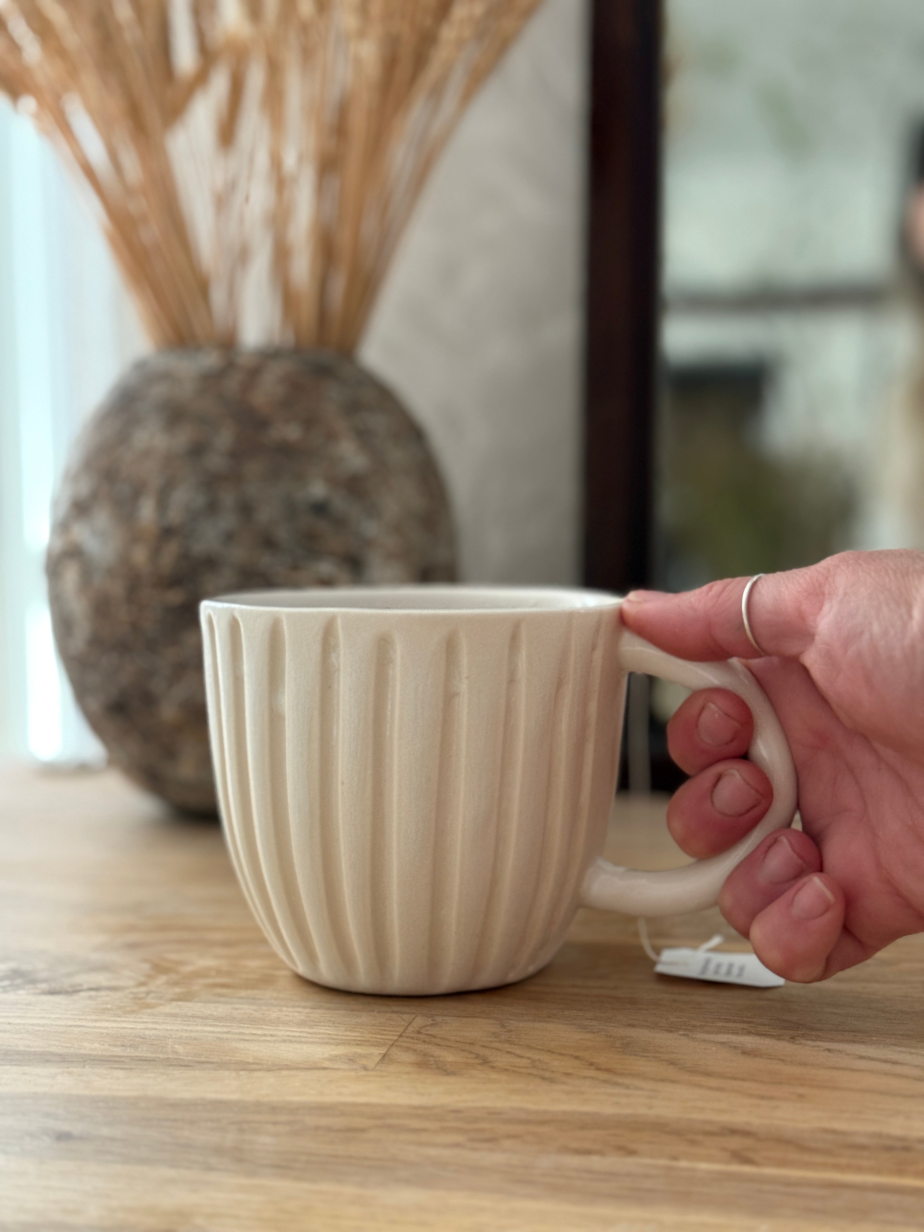 Handmade ceramic coffee mug with hand-carved vertical column lines and a glossy white interior.