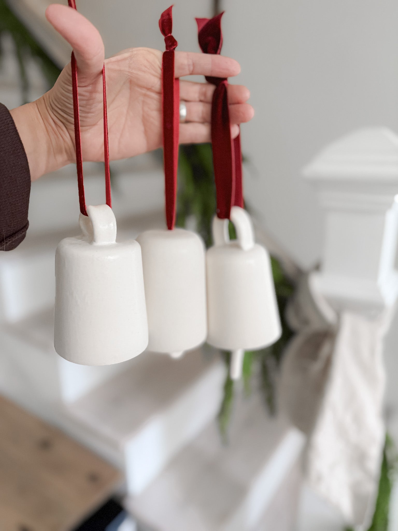 Handmade ceramic holiday bell ornament with a white eggshell finish and red velvet ribbon