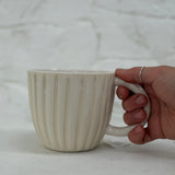 Handmade ceramic coffee mug with hand-carved vertical column lines and a glossy white interior.