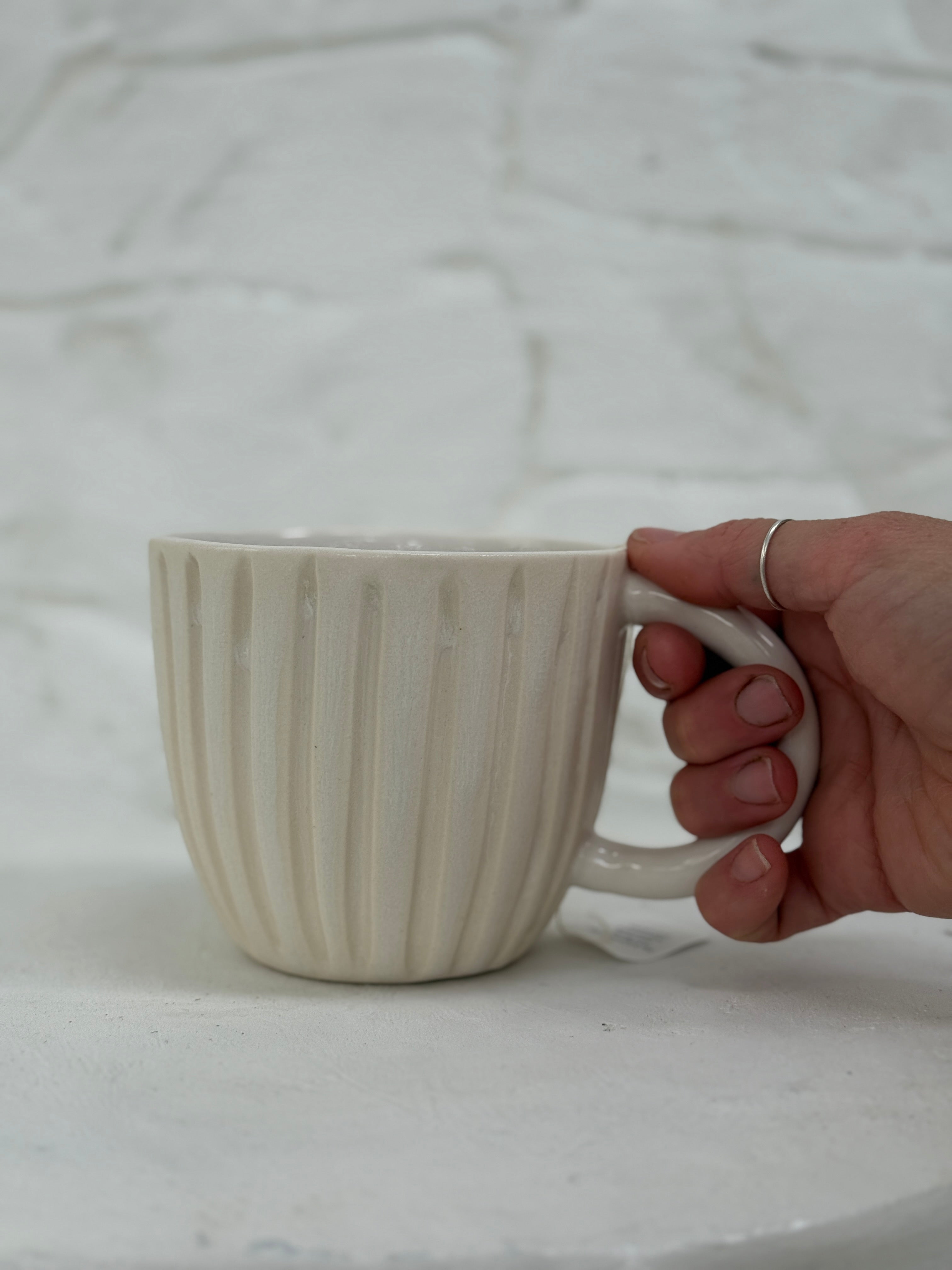 Handmade ceramic coffee mug with hand-carved vertical column lines and a glossy white interior.