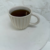 Handmade ceramic coffee mug with hand-carved vertical column lines and a glossy white interior.