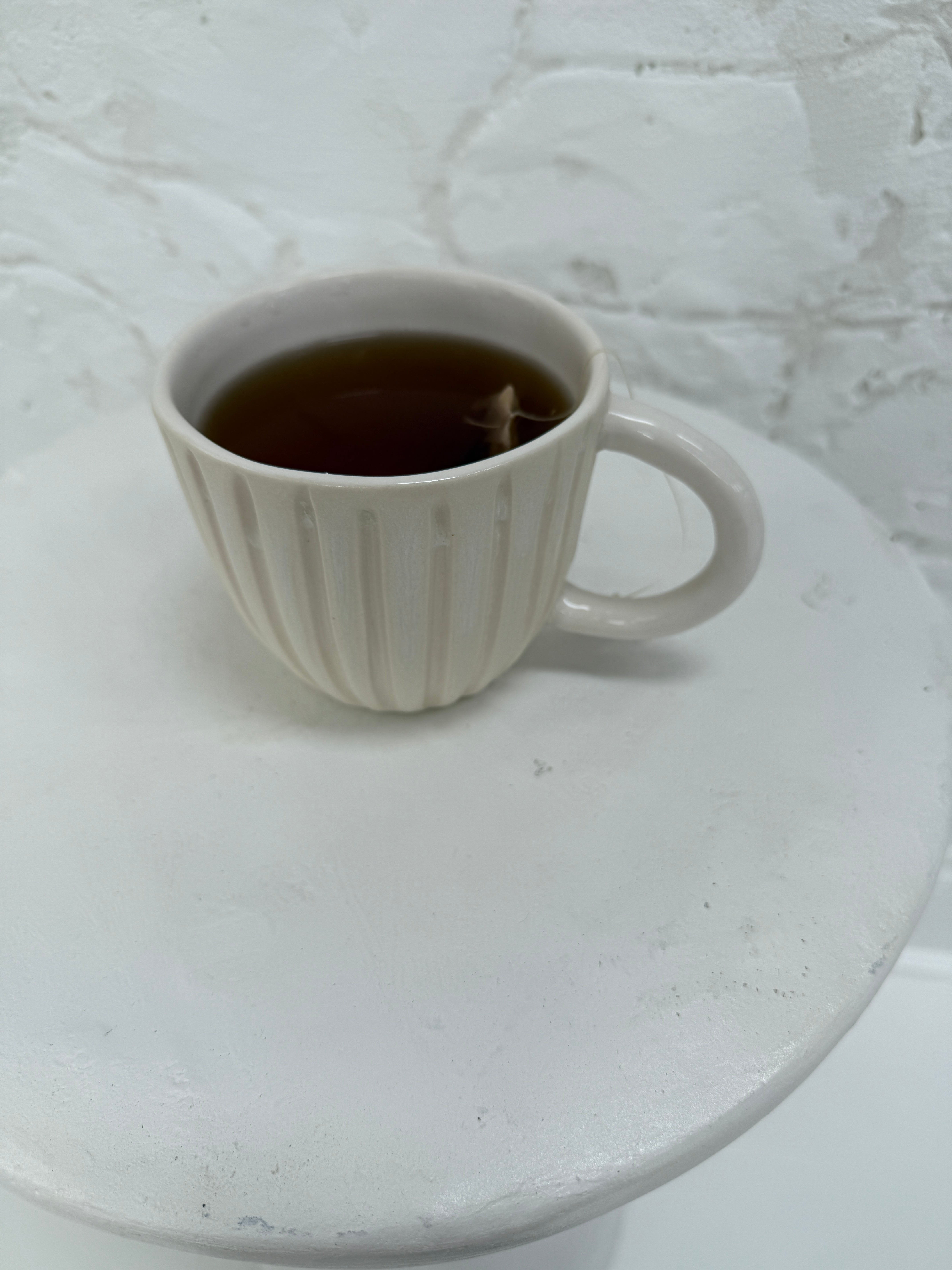 Handmade ceramic coffee mug with hand-carved vertical column lines and a glossy white interior.