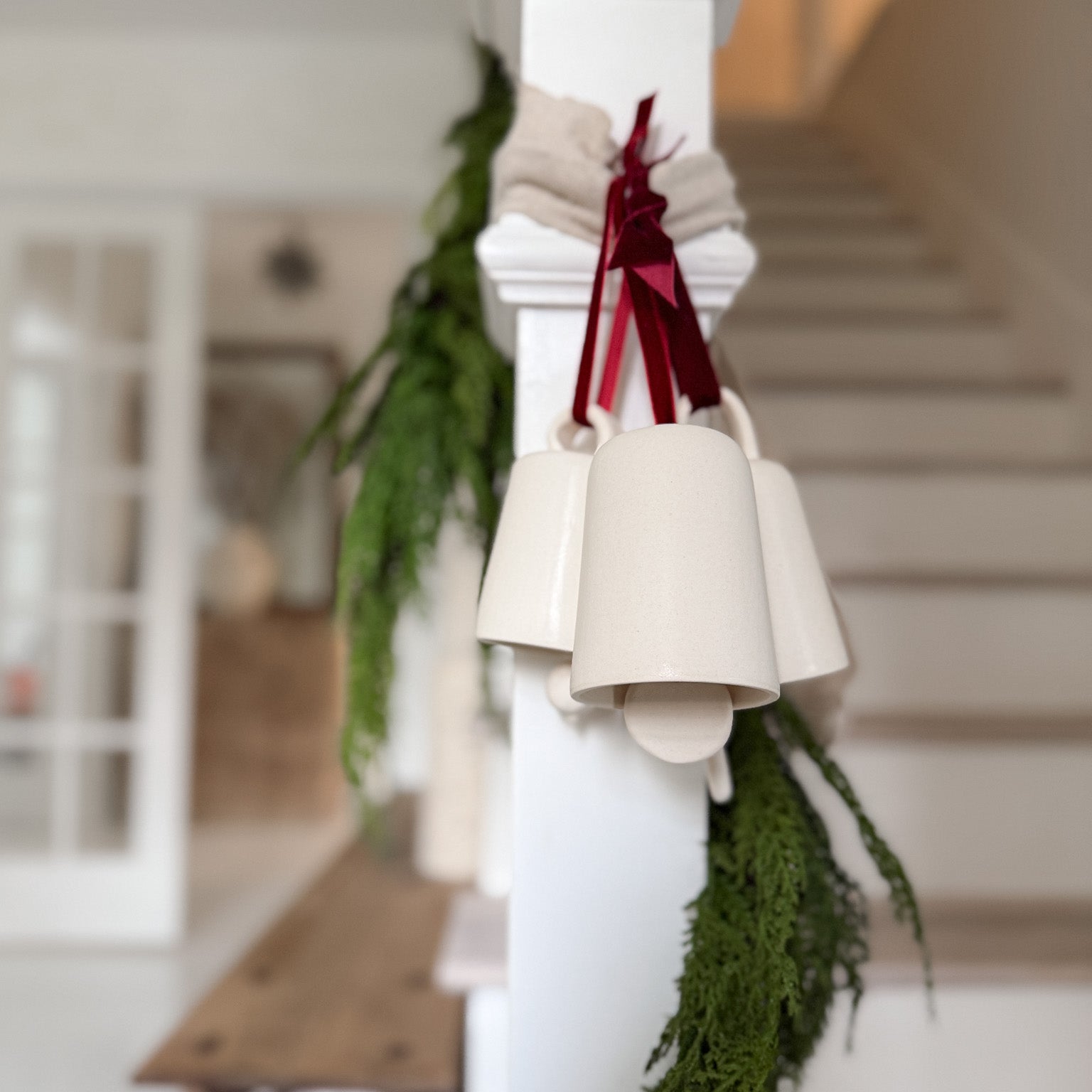 Handmade ceramic holiday bell ornament with a white eggshell finish and red velvet ribbon