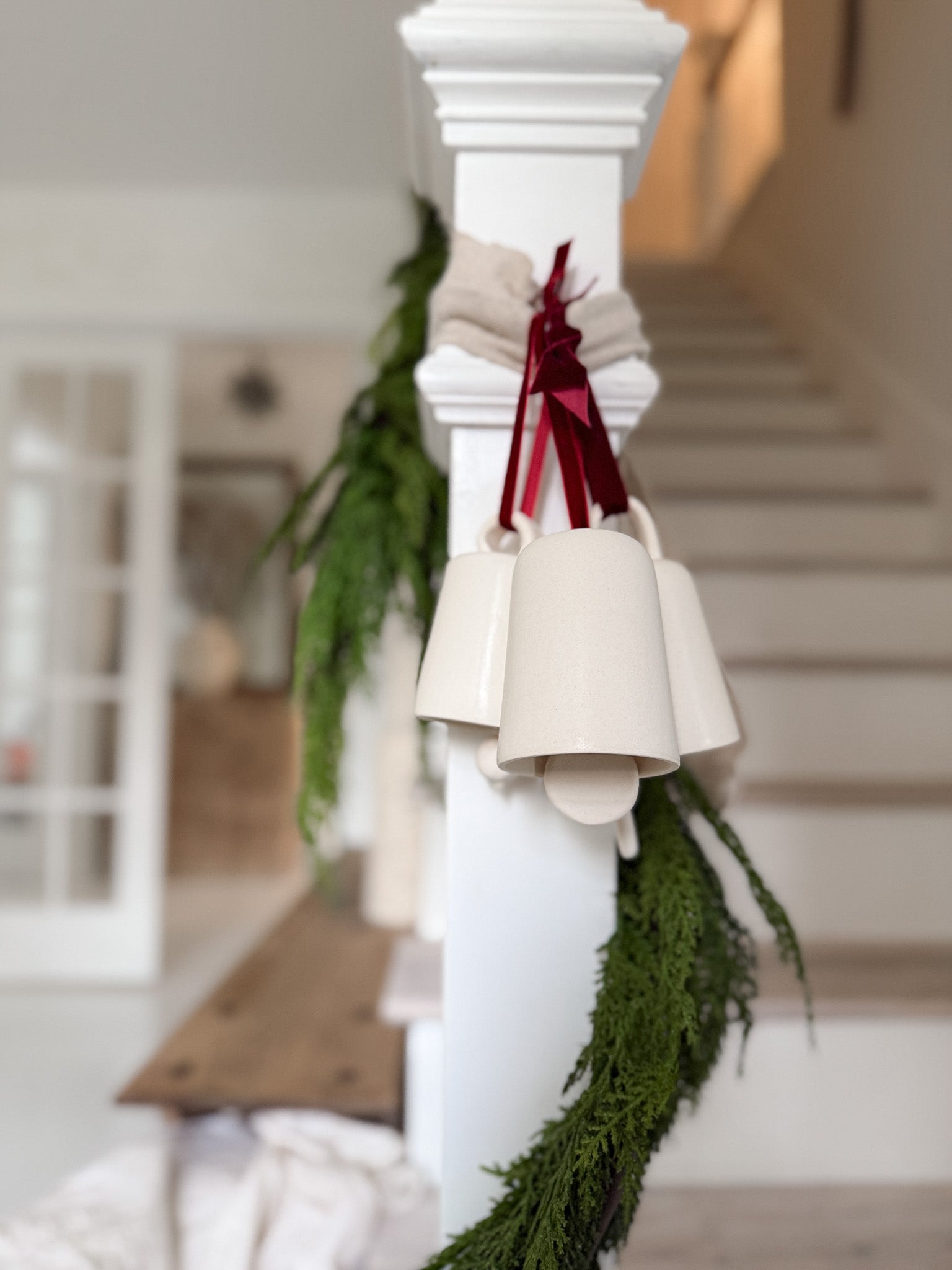 Handmade ceramic holiday bell ornament with a white eggshell finish and red velvet ribbon