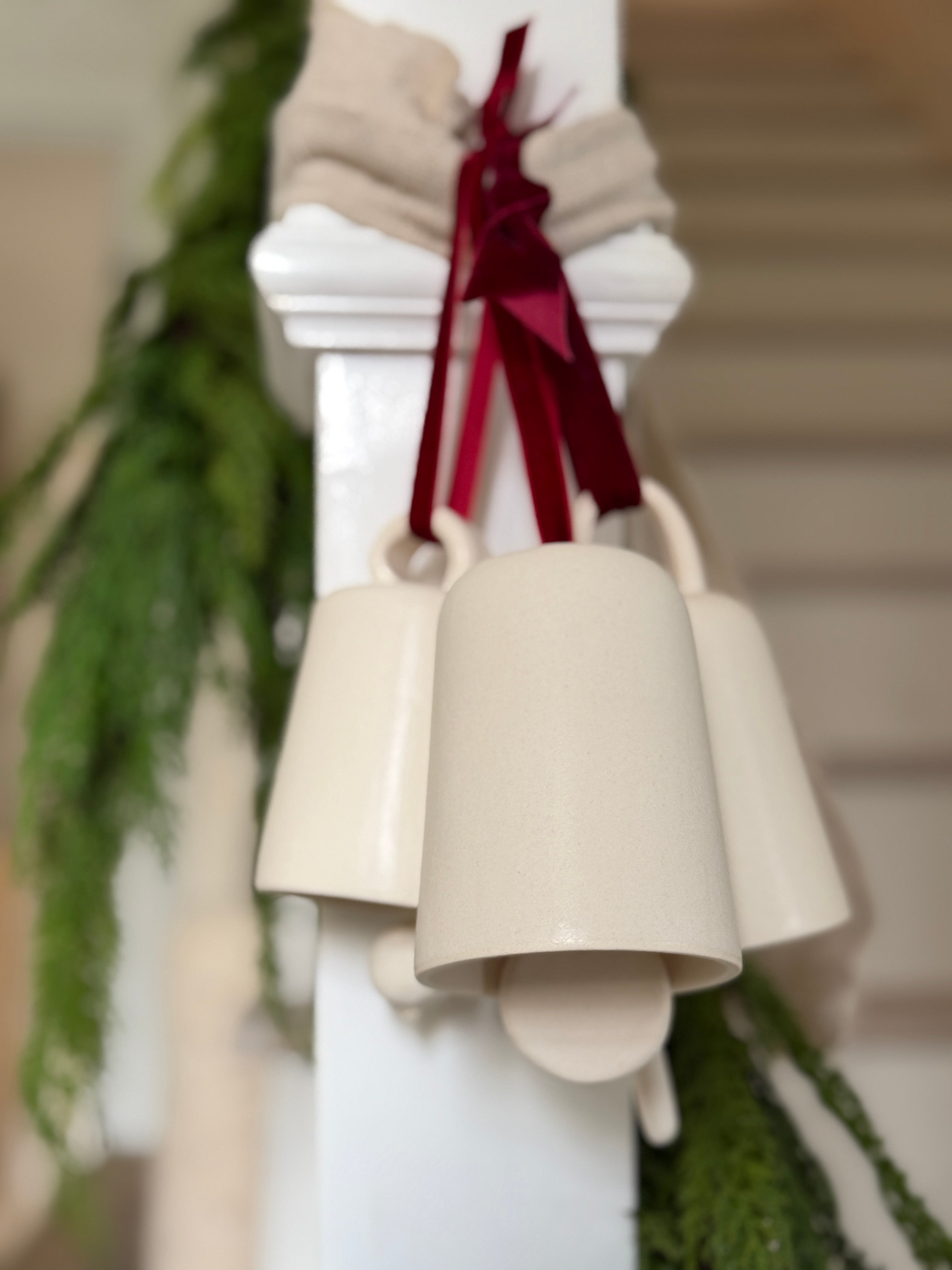 Handmade ceramic holiday bell ornament with a white eggshell finish and red velvet ribbon