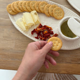 Handmade ceramic servingware with hand-carved line texture — oval platter, dip bowls, and a spread knife.