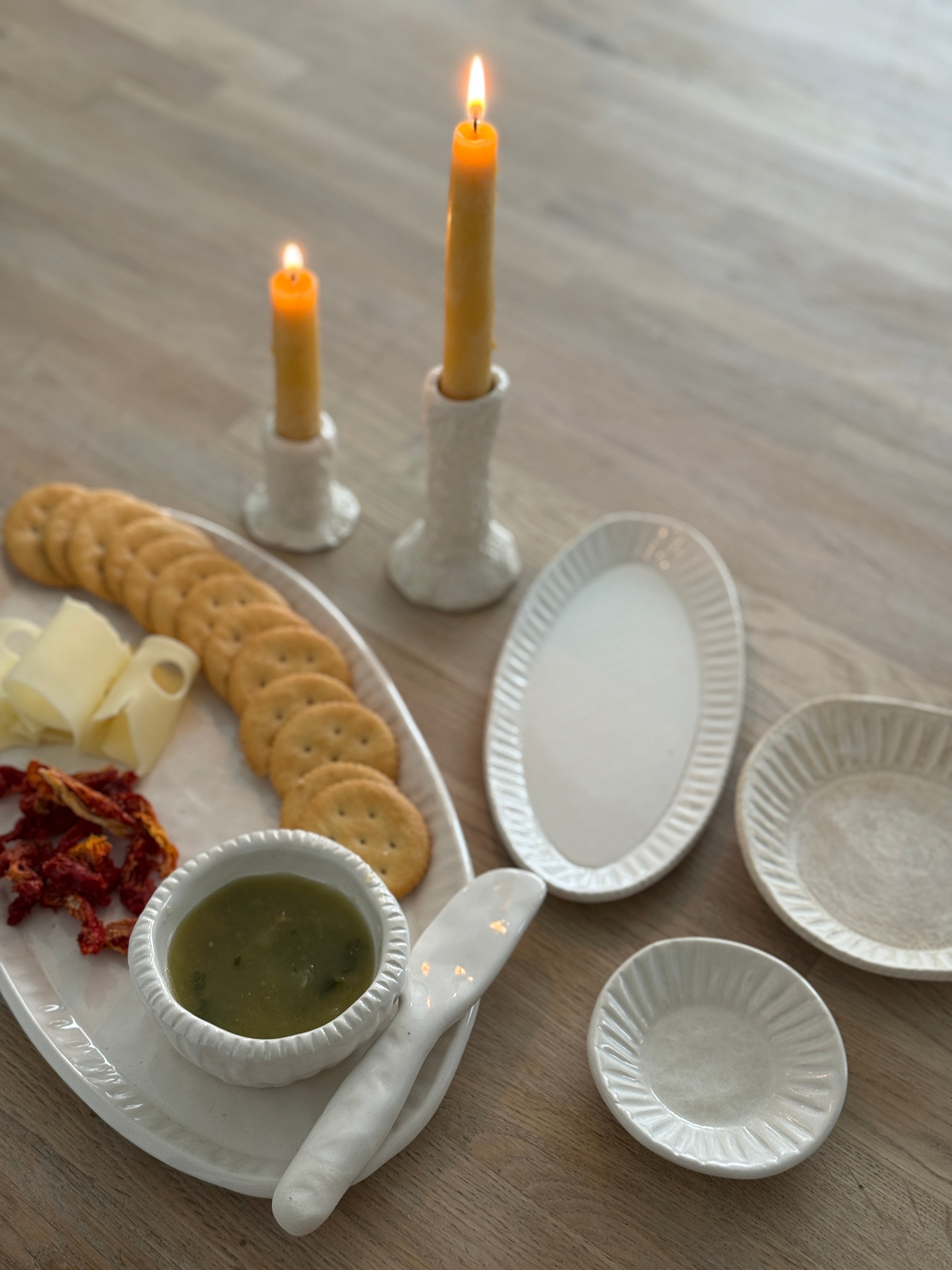 Handmade ceramic servingware with hand-carved line texture — oval platter, dip bowls, and a spread knife.