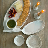 Handmade ceramic servingware with hand-carved line texture — oval platter, dip bowls, and a spread knife.