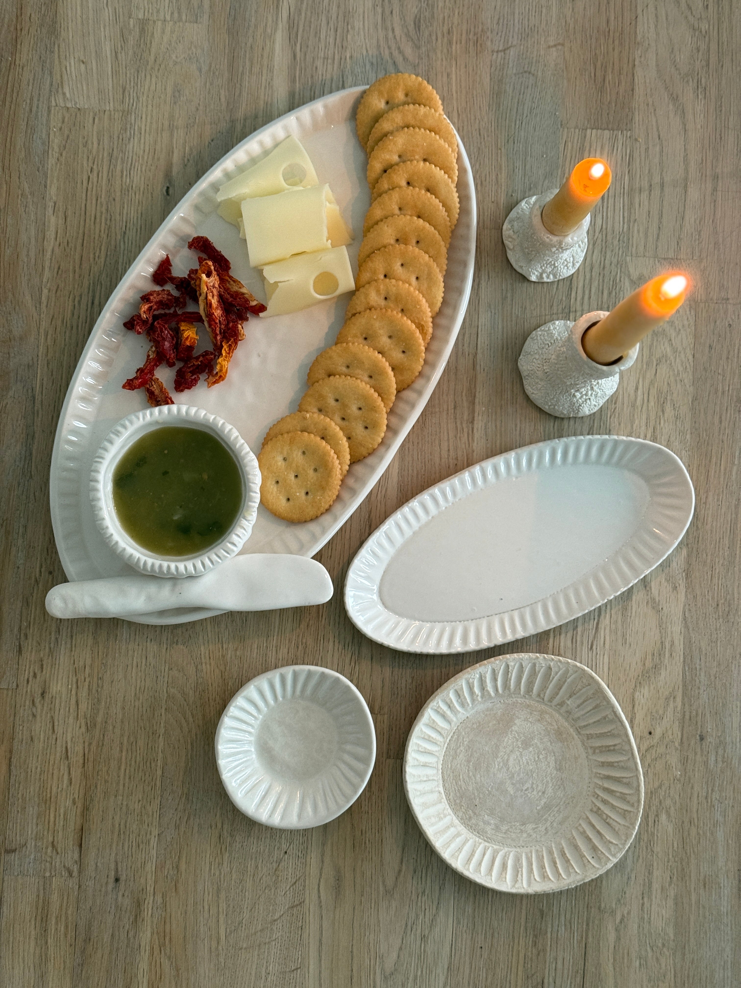 Handmade ceramic servingware with hand-carved line texture — oval platter, dip bowls, and a spread knife.