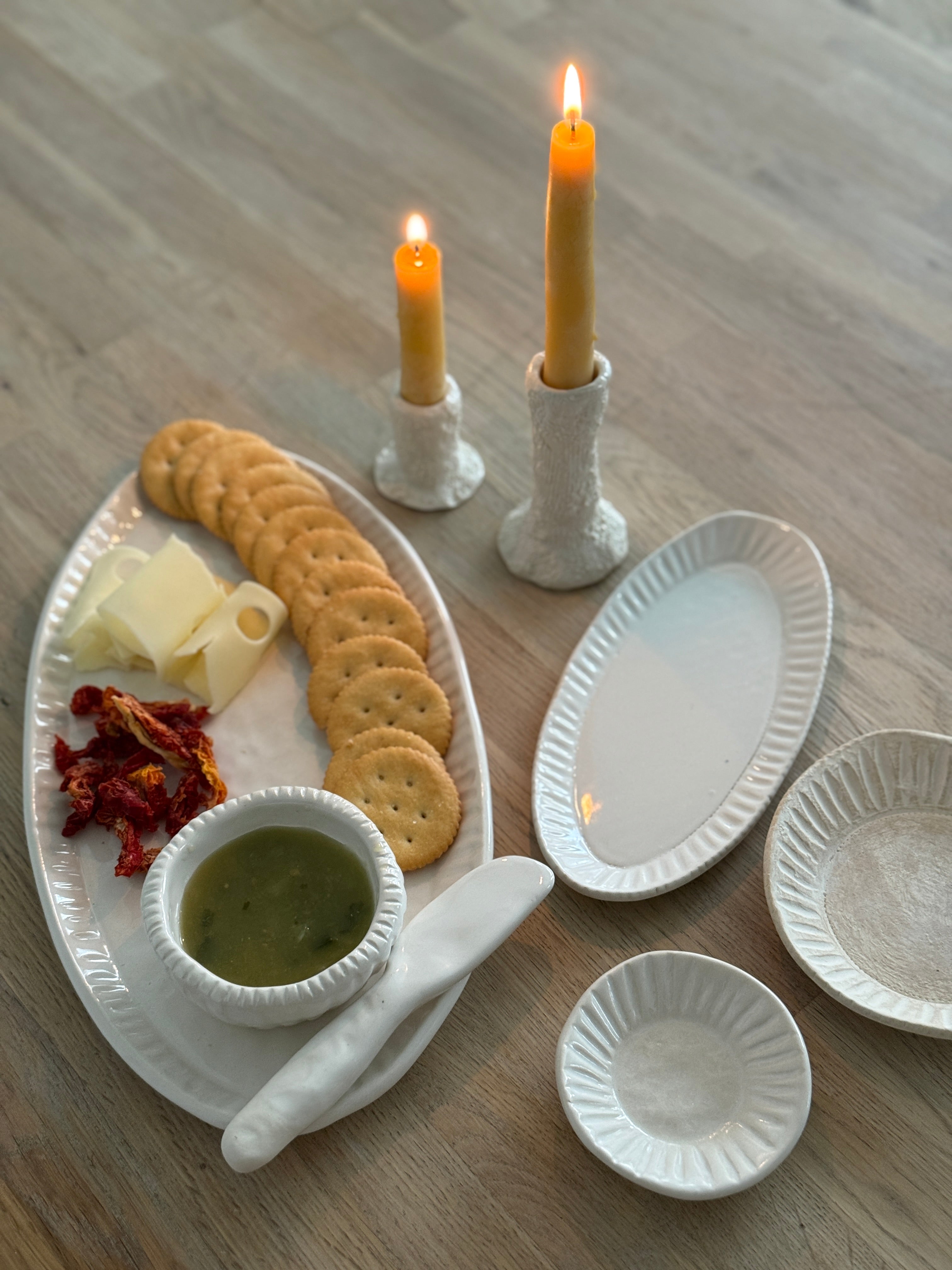 Handmade ceramic servingware with hand-carved line texture — oval platter, dip bowls, and a spread knife.