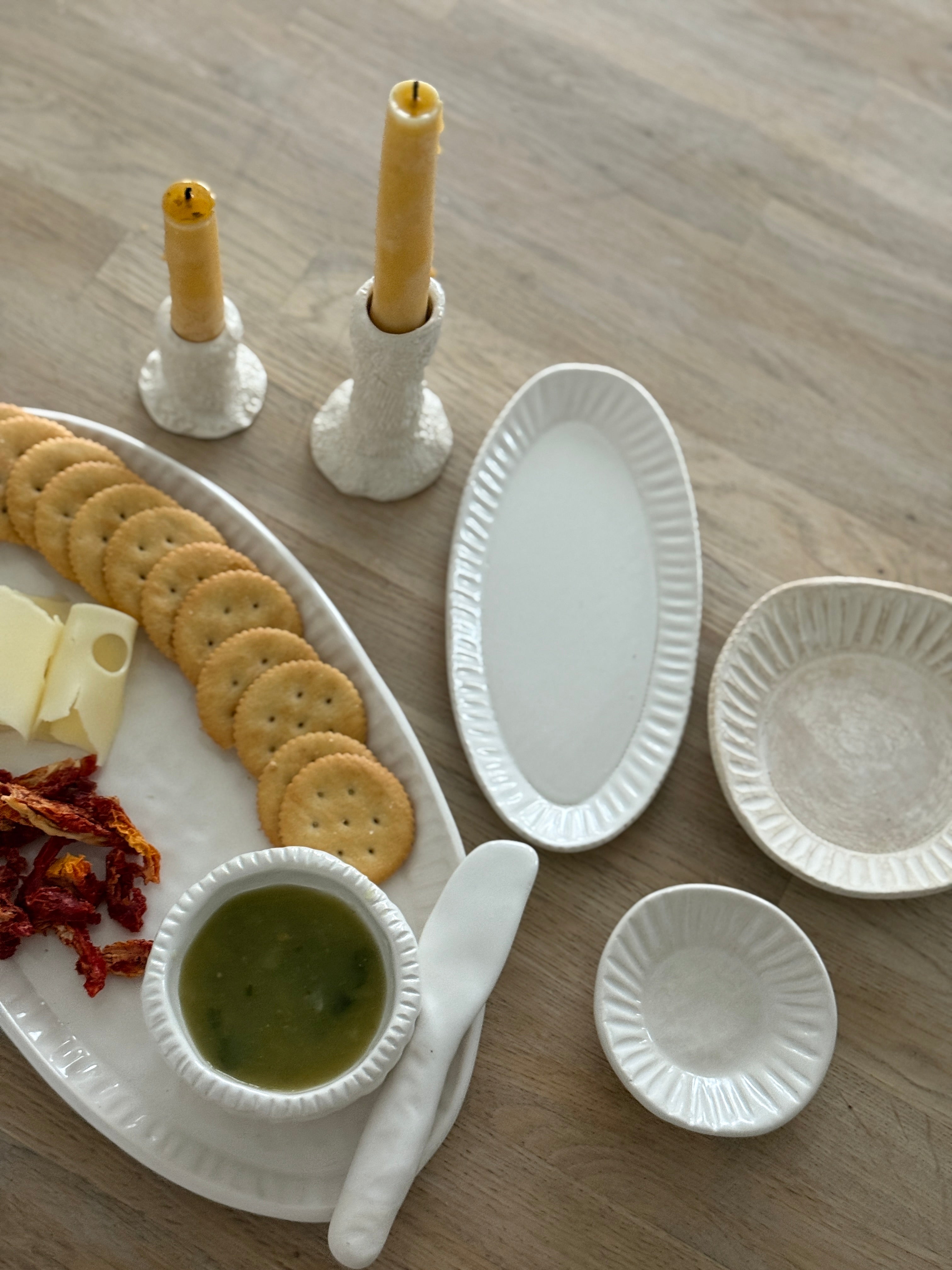 Handmade ceramic servingware with hand-carved line texture — oval platter, dip bowls, and a spread knife.