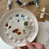 Handmade ceramic watercolor paint palette with mixing wells, a small water cup, and a brush holder.