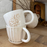 Handmade ceramic coffee mug with hand-carved vertical column lines and a glossy white interior.
