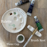 Handmade ceramic watercolor paint palette with mixing wells, a small water cup, and a brush holder.