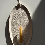 Oval ceramic wall sconce holding a taper candle, hung by natural rope