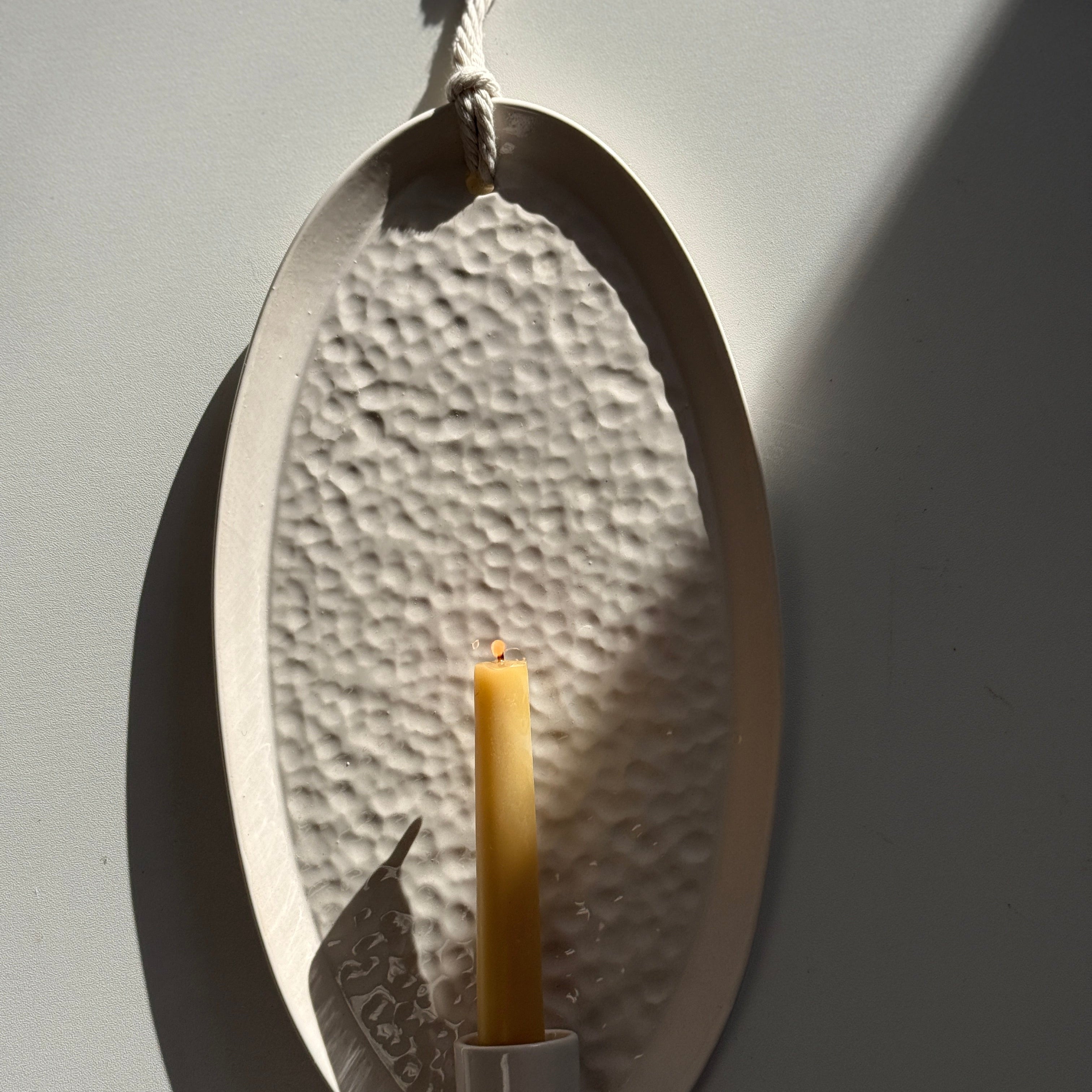 Oval ceramic wall sconce holding a taper candle, hung by natural rope