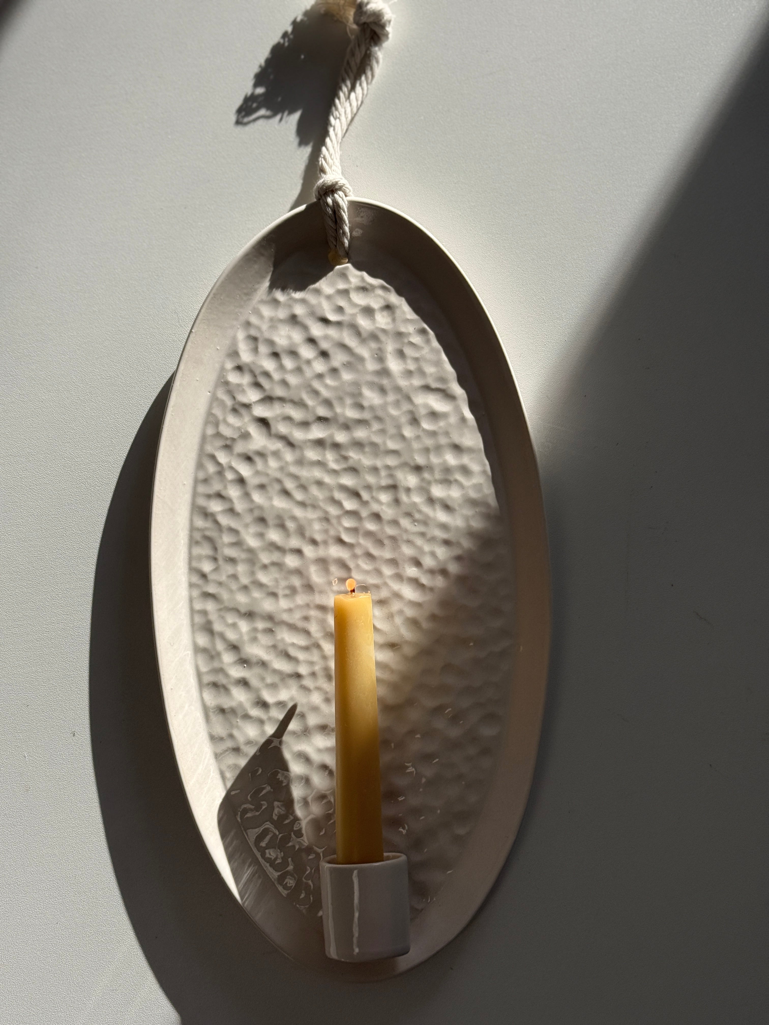Oval ceramic wall sconce holding a taper candle, hung by natural rope