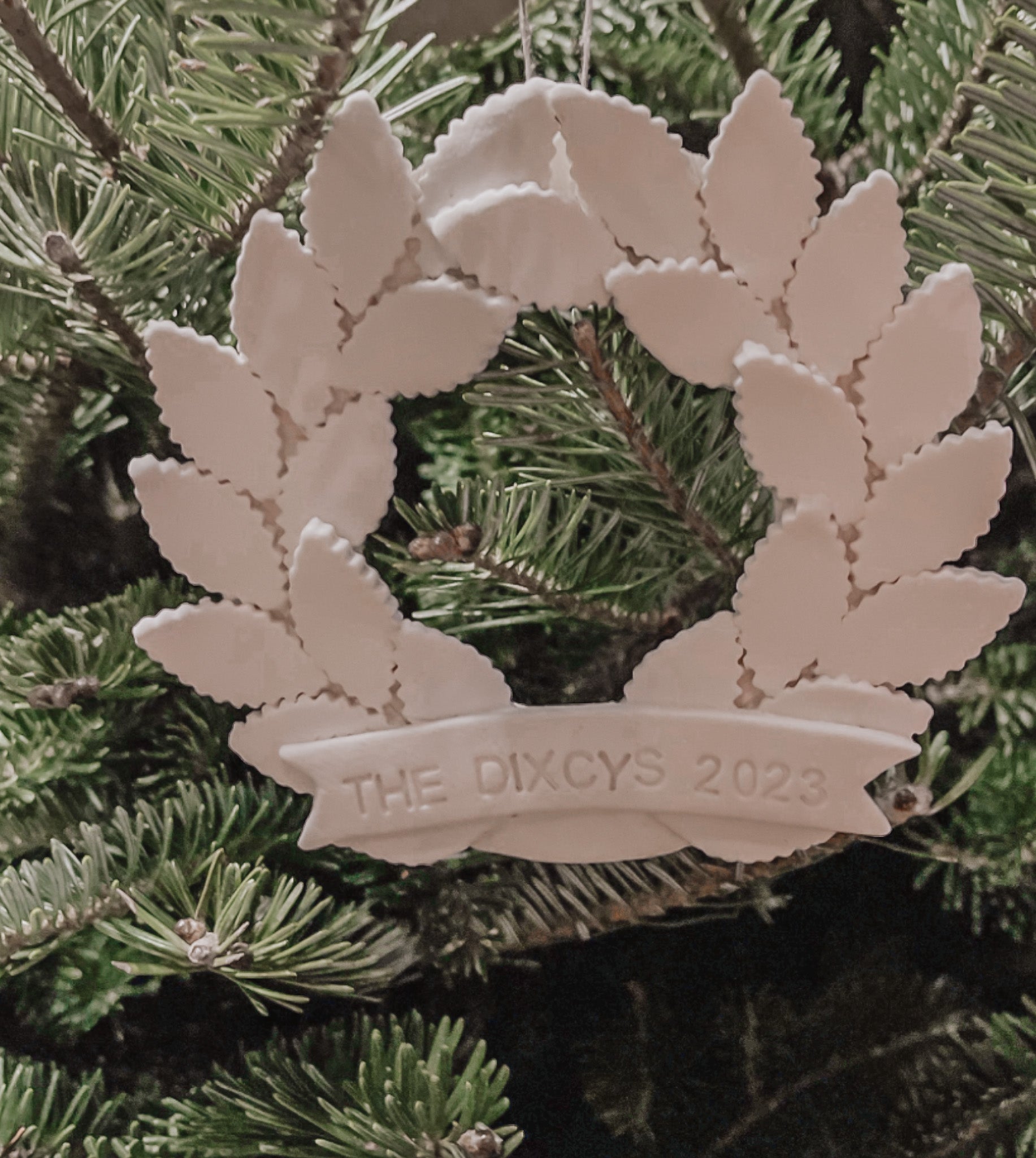 Personalized porcelain laurel wreath ornament with a gloss-white glaze and custom name on linen twine