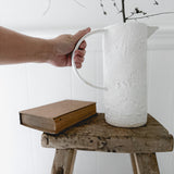 Oversized-handle ceramic pitcher styled with fresh flowers on a counter