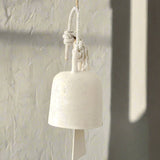 Handmade ceramic barrel hanging bell in textured white glaze, suspended from a rope