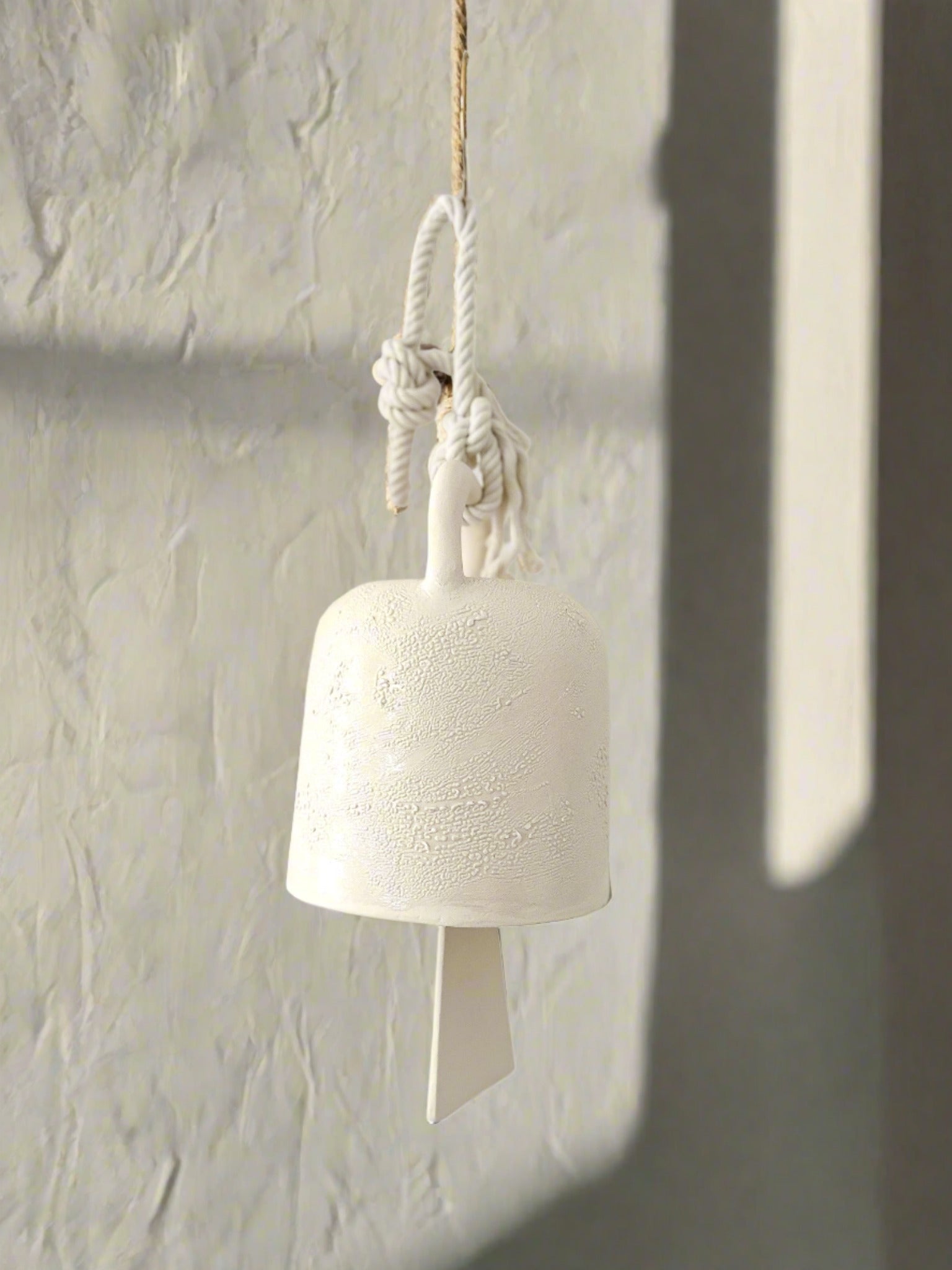 Handmade ceramic barrel hanging bell in textured white glaze, suspended from a rope