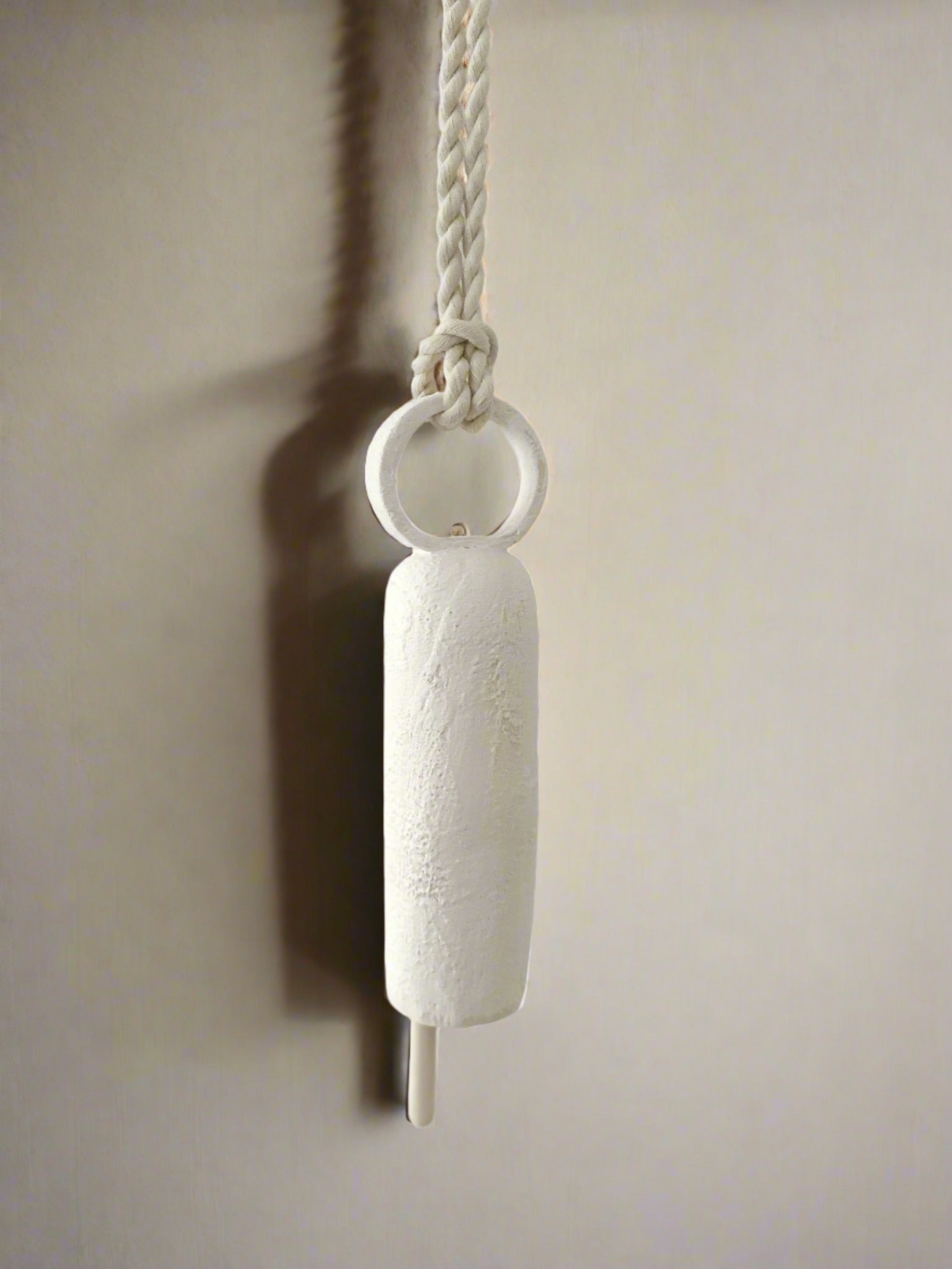 Handmade neutral-glaze ceramic bell with a long handle, detail view