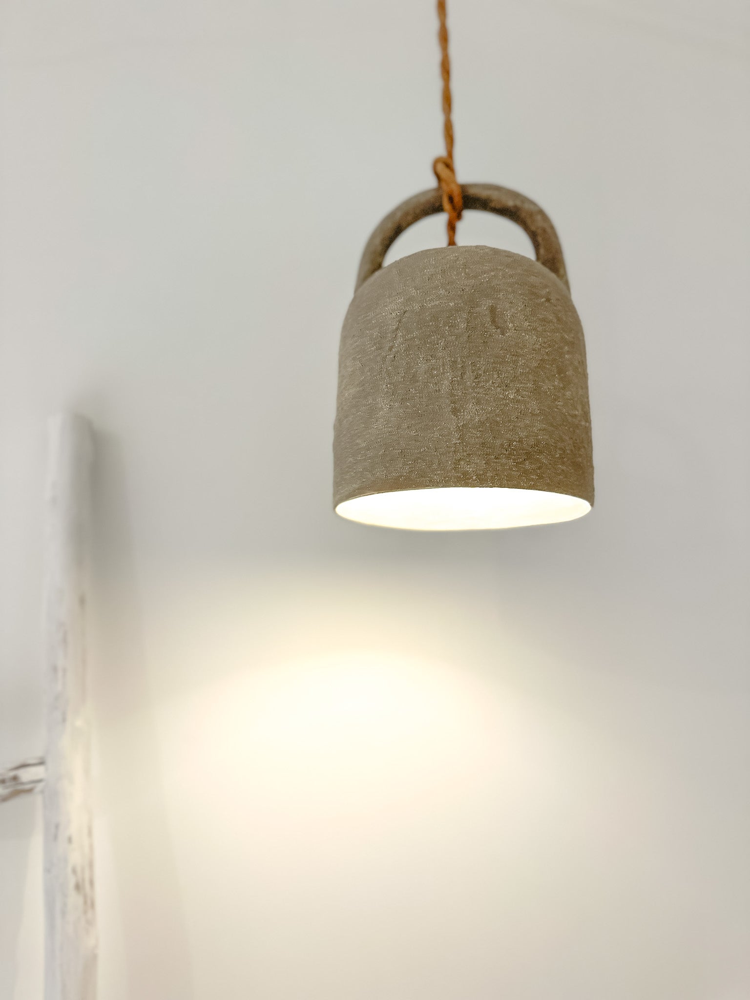 A beige barrel-shaped pendant light hanging from a cord, with light shining from the top.