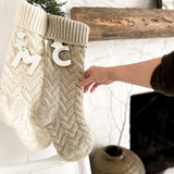 Knitted Christmas stocking with ceramic personalization hung on a mantel