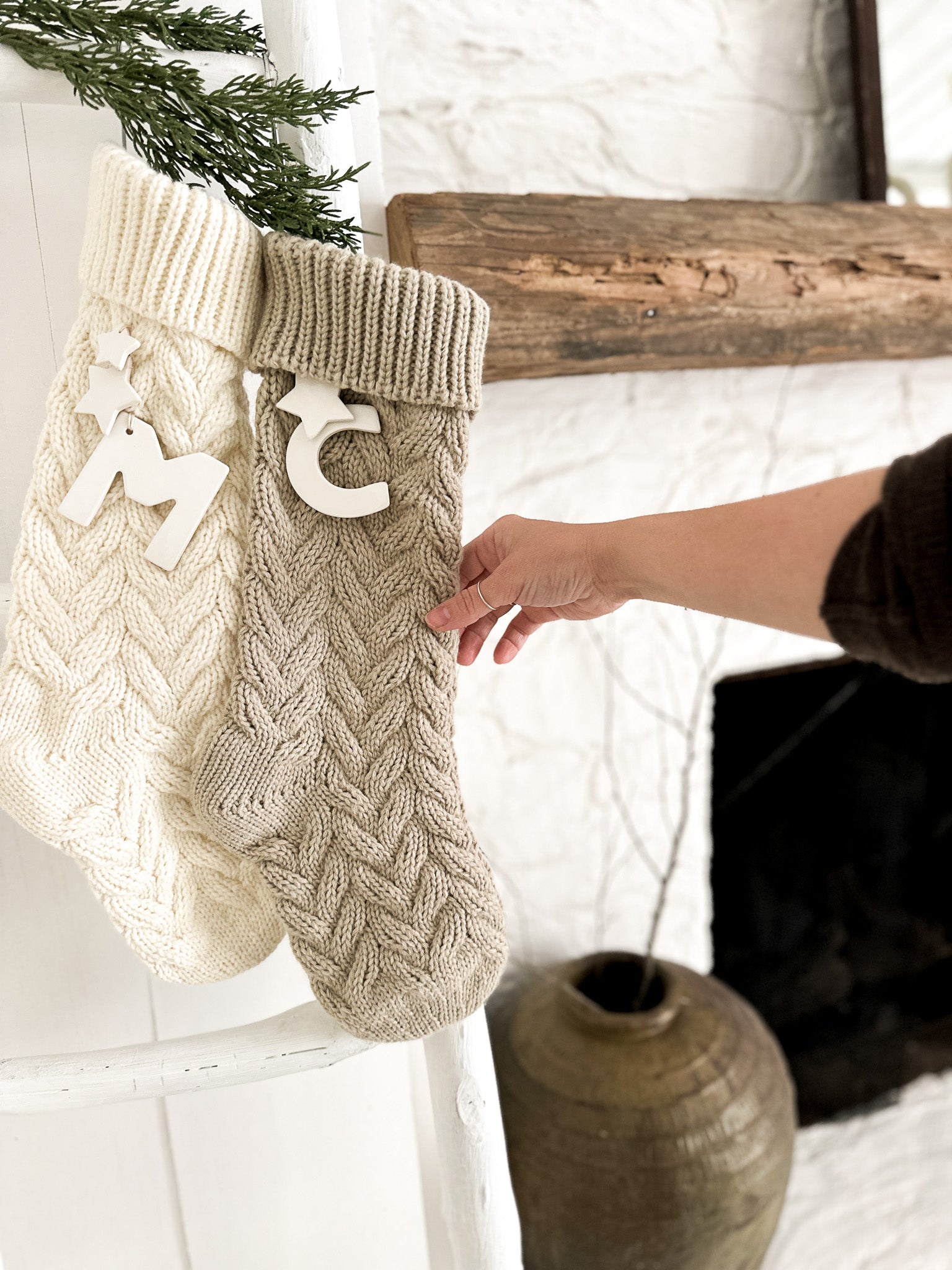 Knitted Christmas stocking with ceramic personalization hung on a mantel