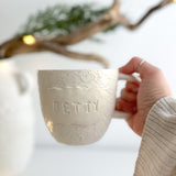 Handmade personalized deep ceramic mug with a glossy white floral-lace textured plaque