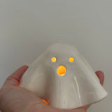 Handmade ceramic ghost luminary glowing softly with an LED tealight candle.