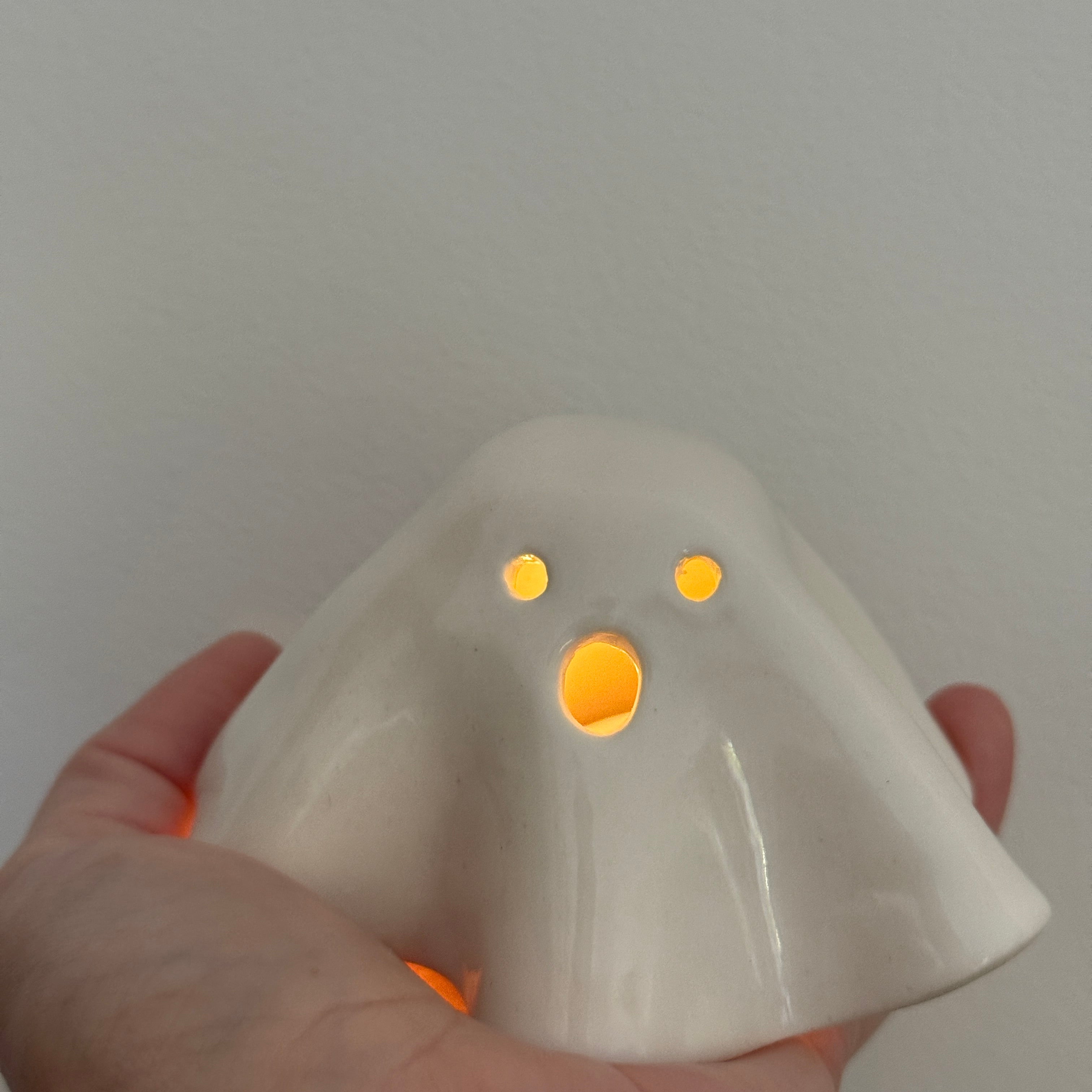 Handmade ceramic ghost luminary glowing softly with an LED tealight candle.