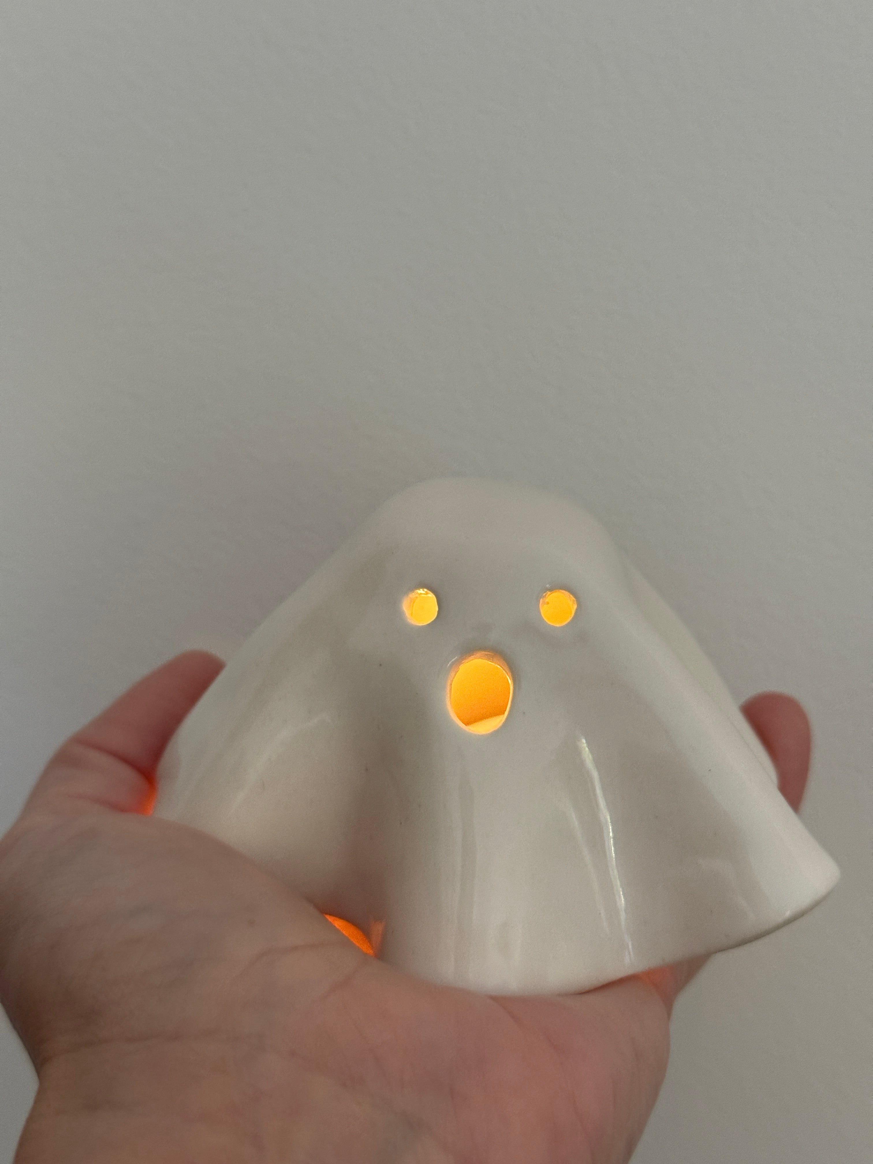 Handmade ceramic ghost luminary glowing softly with an LED tealight candle.