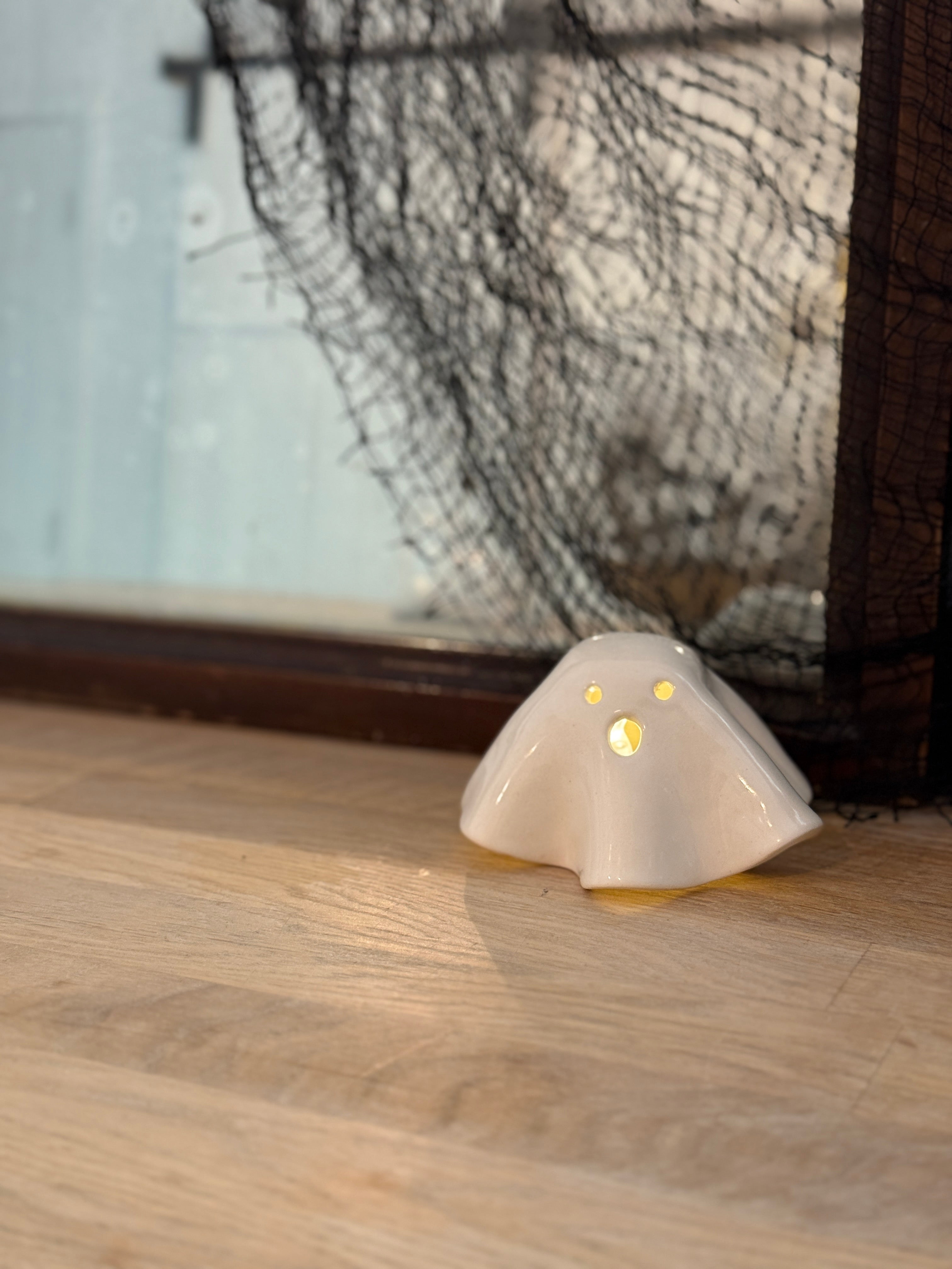 Handmade ceramic ghost luminary glowing softly with an LED tealight candle.