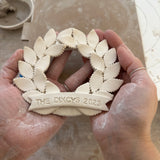 Personalized porcelain laurel wreath ornament with a gloss-white glaze and custom name on linen twine