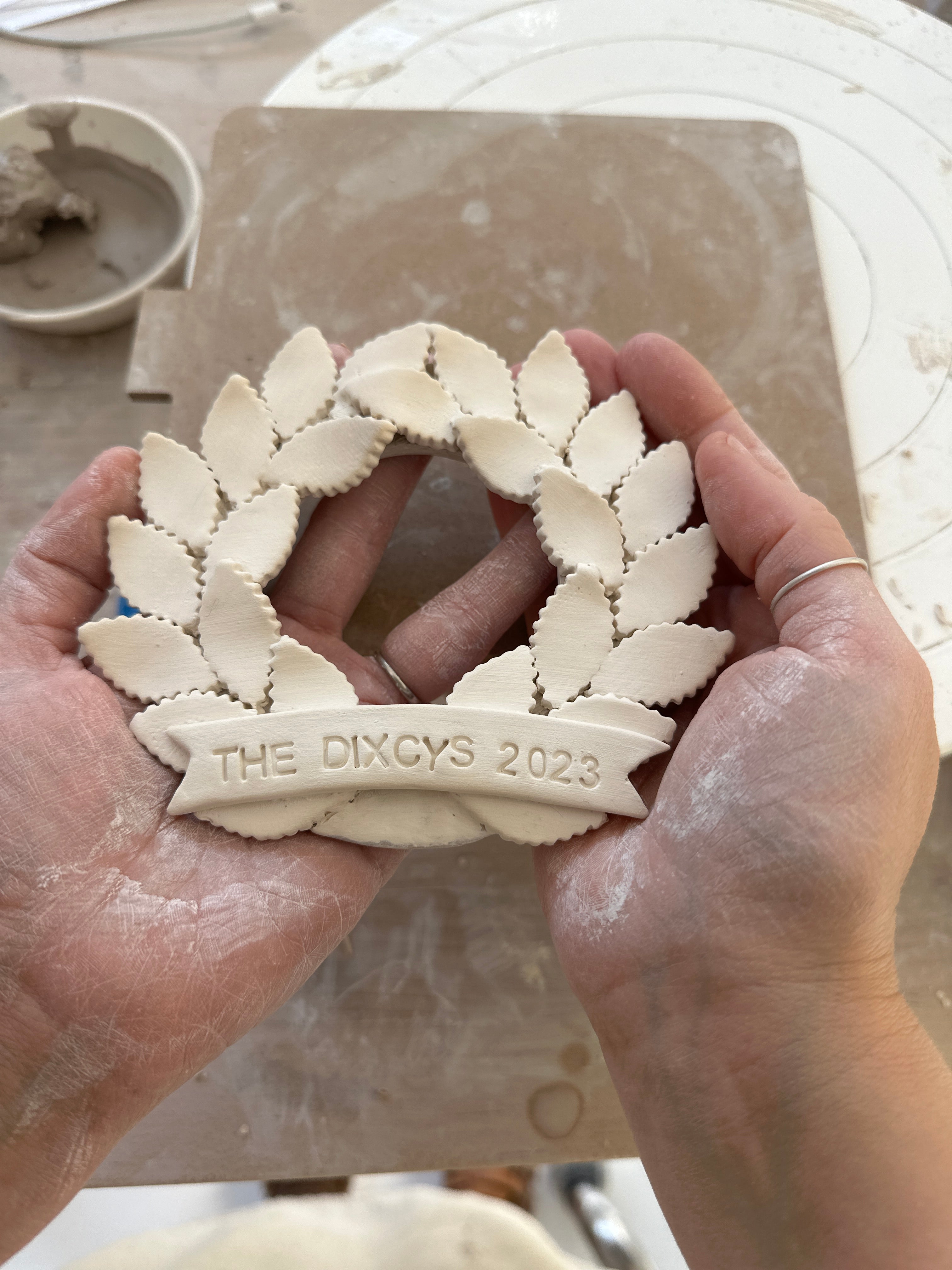 Personalized porcelain laurel wreath ornament with a gloss-white glaze and custom name on linen twine