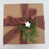 Kraft gift box tied with a rust silk ribbon, greenery, and a small ceramic star gift tag.