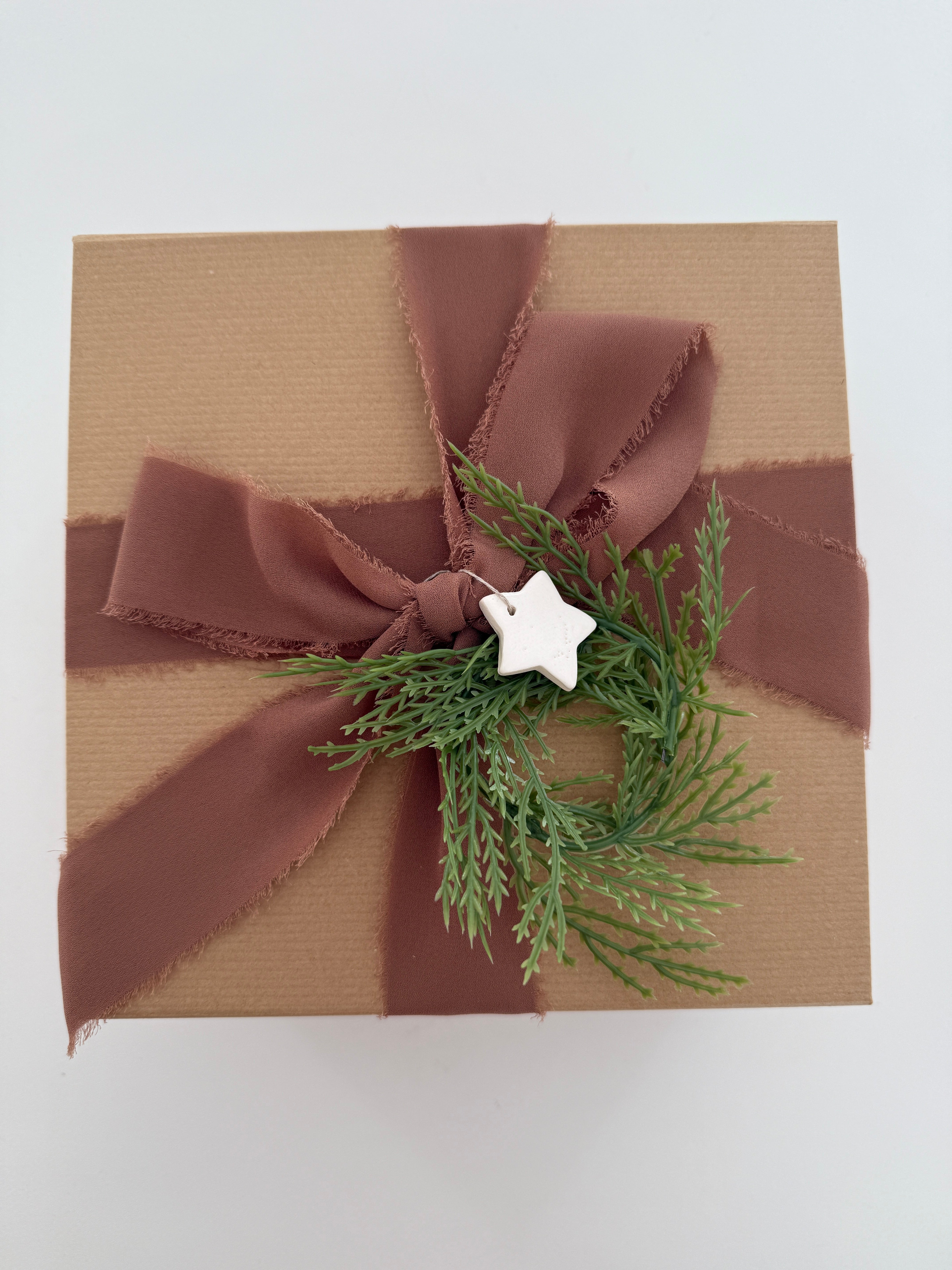 Kraft gift box tied with a rust silk ribbon, greenery, and a small ceramic star gift tag.