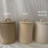 Three handled ceramic kitchen canisters with arch-lift lids shown side by side in Sand, Oat and Matte White finishes.