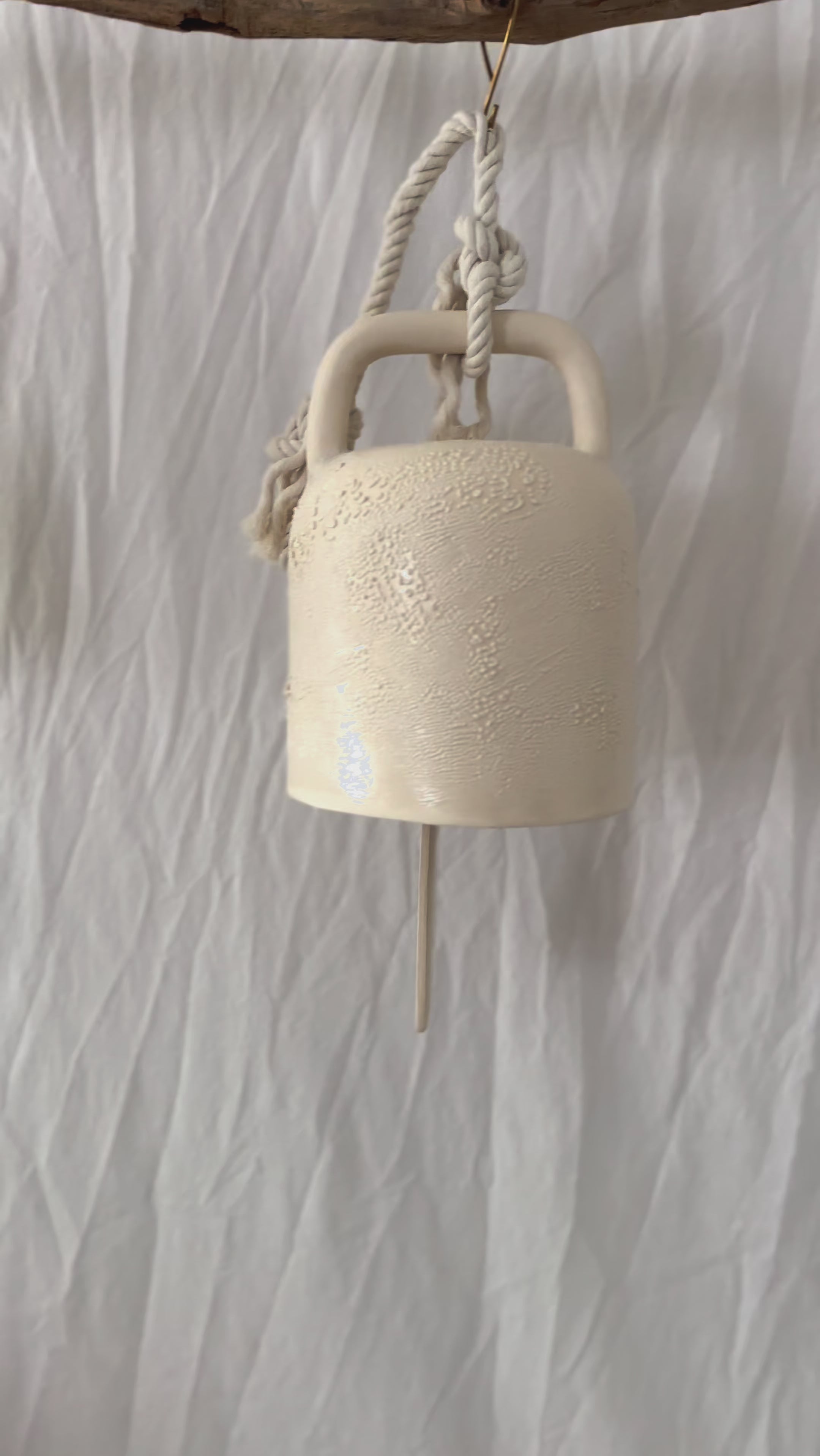 Elegant white ceramic bell with a textured surface for farmhouse style, handmade with care to enhance rustic home decor. This artisanal hanging bell, featuring a durable rope, provides a soothing sound and a timeless aesthetic, making it a wonderful addition to any farmhouse or vintage-inspired space.
