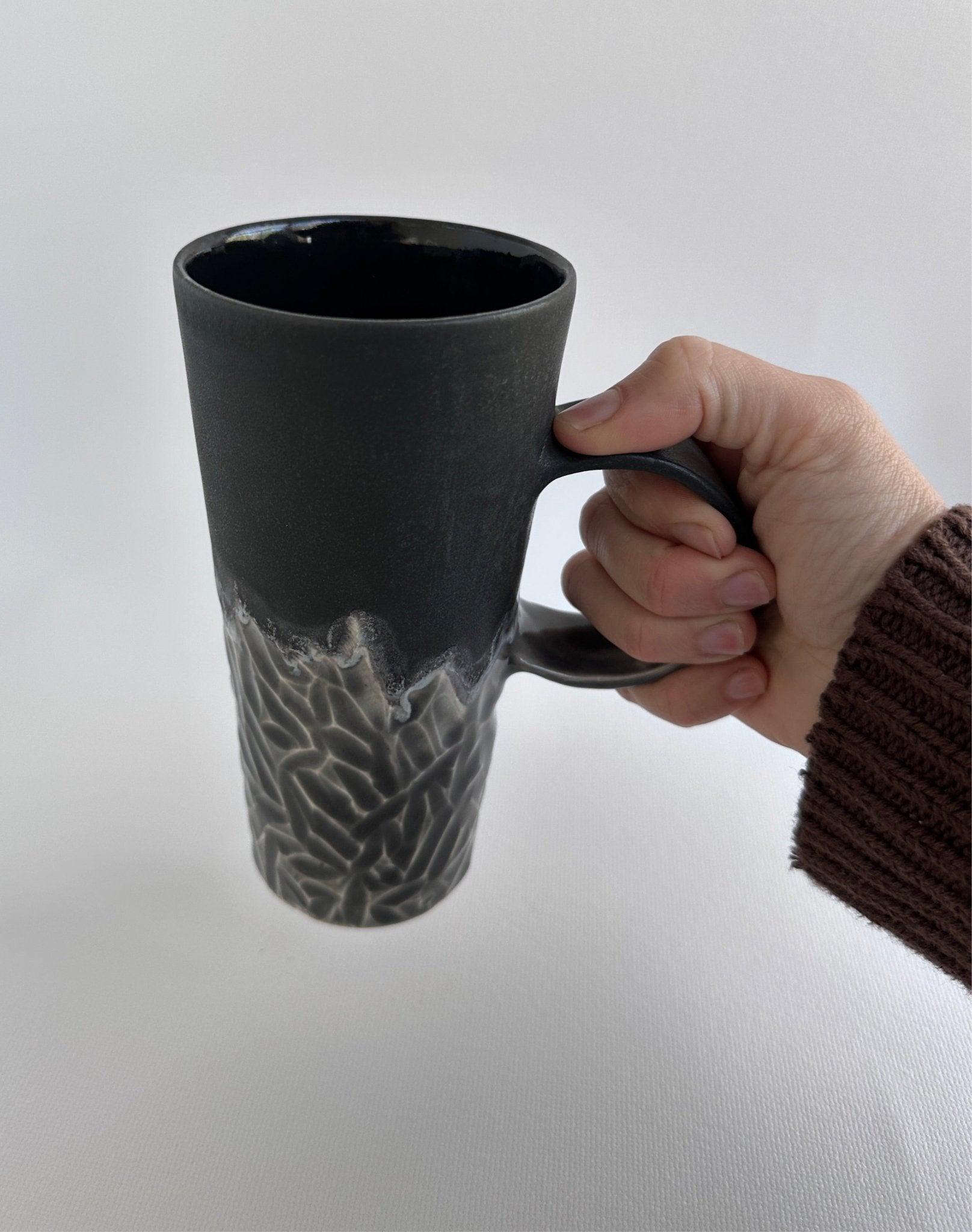Handmade tall hand-carved ceramic mug in frosted black with a smokey-grey carved texture and glossy black interior
